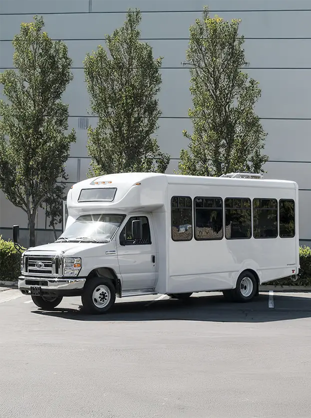 white passenger van parked in front of a building and trees in a parking lot