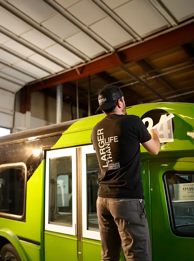 tech working on laying a vehicle graphic on a bus
